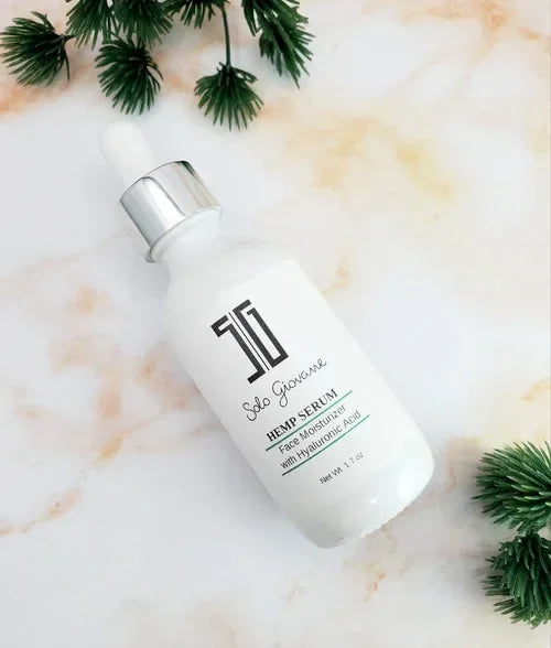 SG Hemp Serum bottle with dropper on marble surface surrounded by green pine branches.