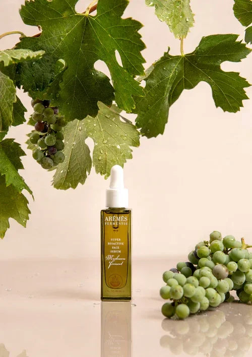 Super Bioactive Face Serum bottle with fresh green grapes and grapevine leaves with water droplets background