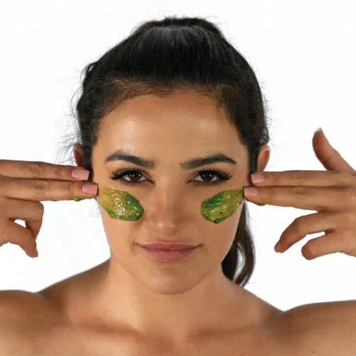 Woman applying green Detoxifying Exfoliating Mask to her cheeks with fingers against a white background